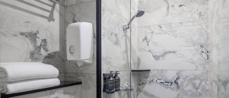 Un baño moderno con paredes de mármol, cabina de ducha de vidrio, un perchero, dispensador de jabón y un cabezal de ducha de mano.