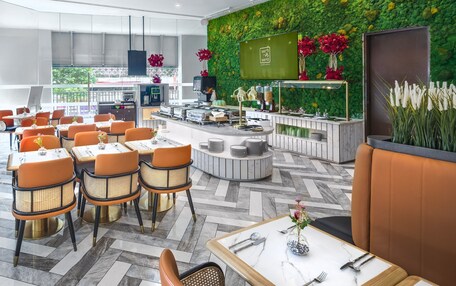 A modern restaurant with a green wall, orange chairs, and a counter with a TV.