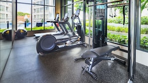 Un gimnasio moderno con cintas de correr, una banca y una máquina de pesas, con amplias ventanas y vistas al exterior con vegetación.