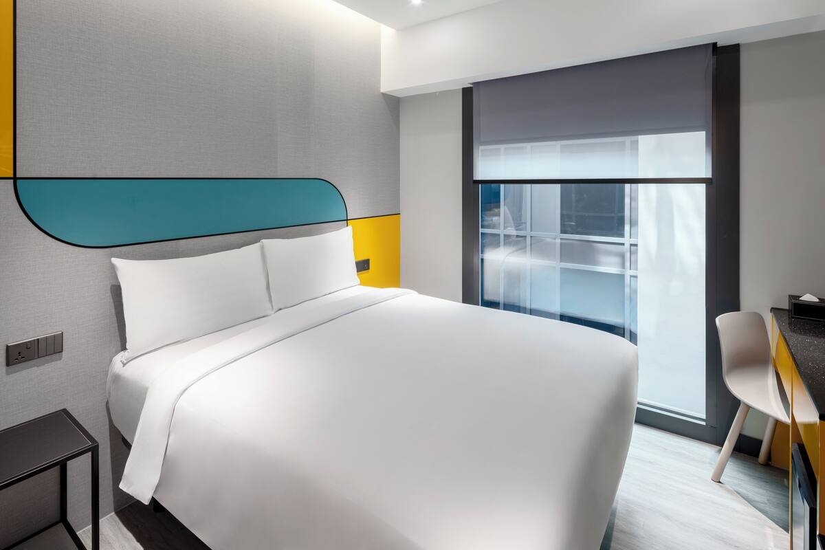 A modern hotel room with a large bed, a desk, and a window with a view.