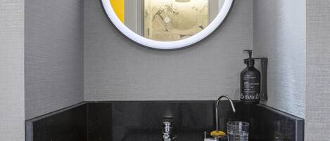 Un baño con un espejo redondo, un lavamanos y una botella de Urban Skincare.