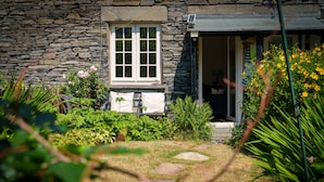 A stone building with a window and a door, surrounded by a garden with various plants and flowers. - Red Robin Cottage -  Garden, Parking and Walk to the Lake (Ambleside)