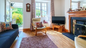 A living room with a sofa, a chair, a TV, a fireplace, and a window with curtains. - Red Robin Cottage -  Garden, Parking and Walk to the Lake (Ambleside)