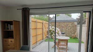 A room with a sliding glass door leading to an outdoor patio area with a wooden deck, a stone wall, and a garden with hydrangeas.