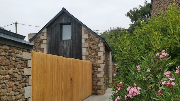 A stone building with a wooden gate, a stone pathway, and pink flowering plants.