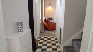 Ein Gang mit Schachbrettmuster, der zu einem Zimmer mit Heizkörper, Stuhl und Lampe führt.