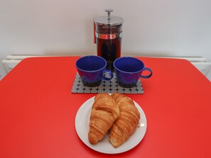 A red table with a plate of croissants, two blue cups, and a coffee press. - White Feathers (Alnwick)