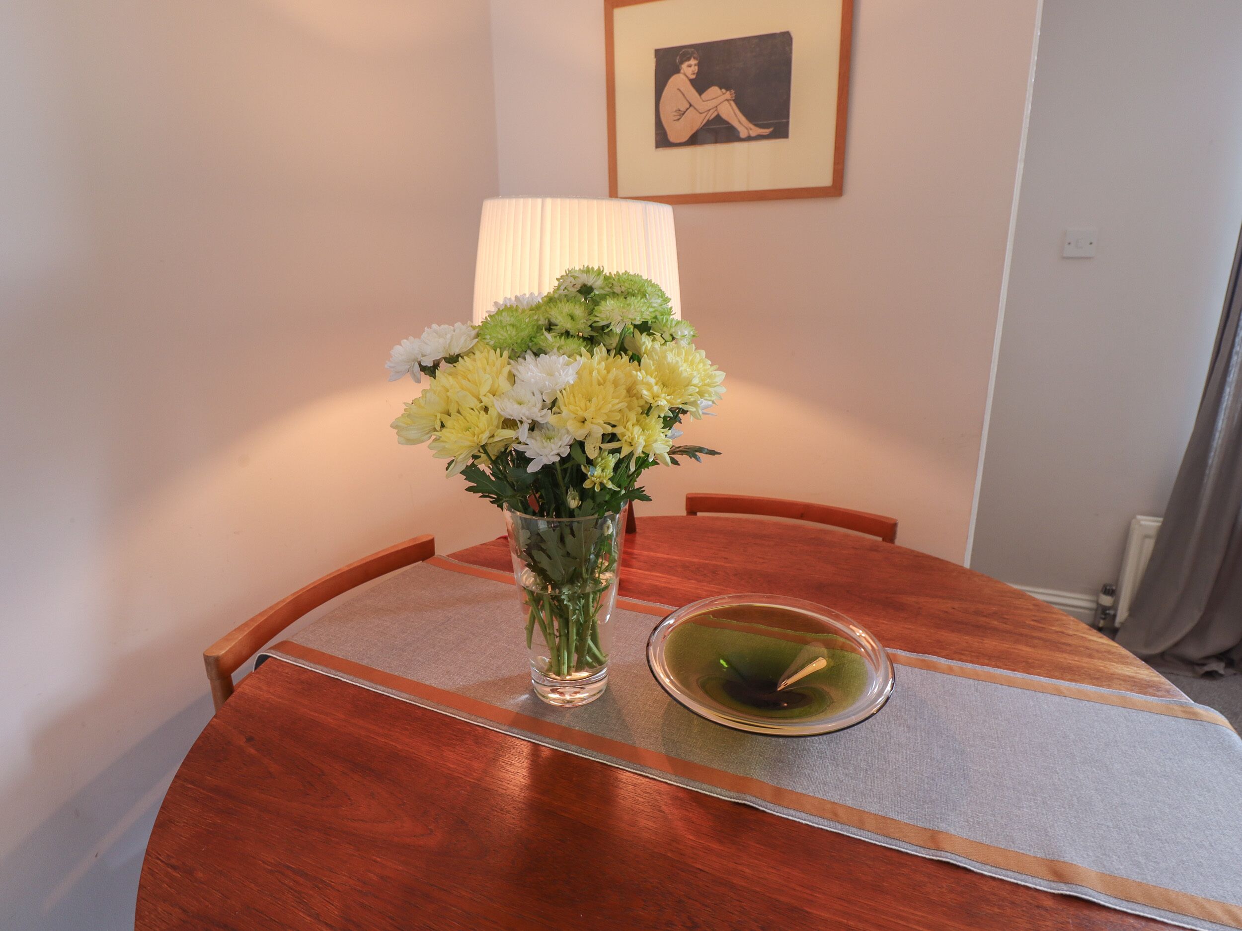 A dining table with a vase of flowers, a candle, and a framed picture on the wall.