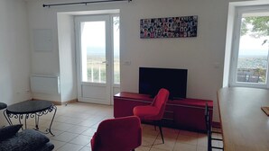 Een woonkamer met een televisie, rode stoelen, een eettafel en een balkon met uitzicht.
