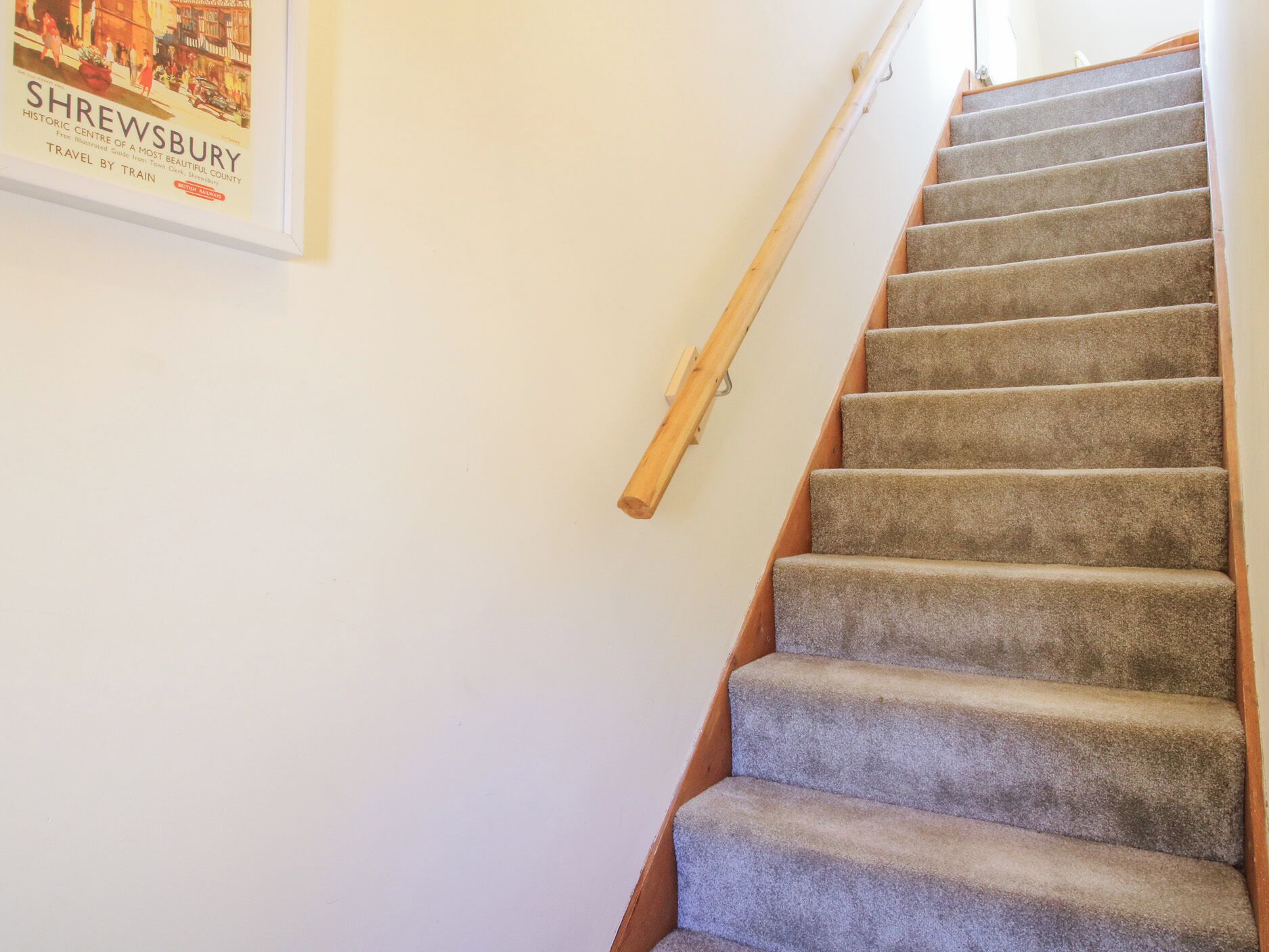 A carpeted staircase with a wooden handrail and a poster on the wall.