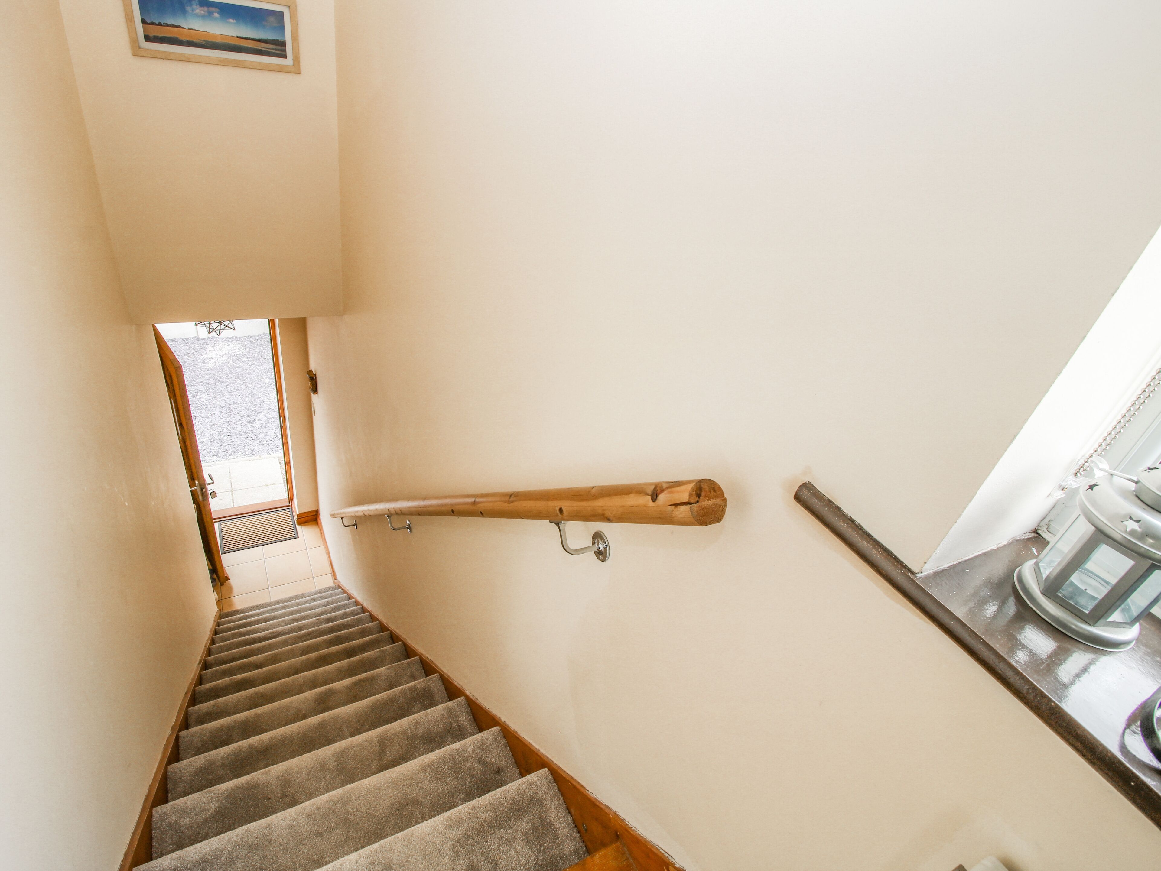A carpeted staircase with a wooden handrail, a picture on the wall, and a window with a view of the outdoors.