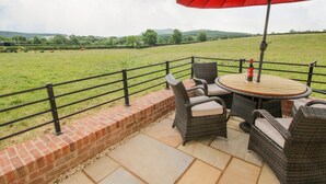 A patio with wicker furniture and a red umbrella, overlooking a grassy field. - Mossy Lodge (Shrewsbury)