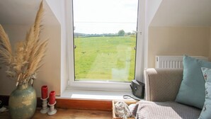A room with a large window, a radiator, a sofa, a vase with dried plants, and a small table with candles. - Mossy Lodge (Shrewsbury)