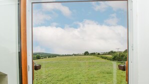 A view through a door of a grassy field with a fence, a clear sky, and distant hills. - Mossy Lodge (Shrewsbury)