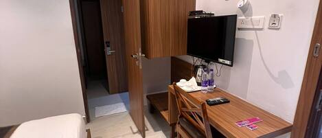 A small, compact room with a wooden desk, a chair, a television, and a bed.