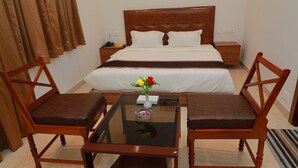 A hotel room with a large bed, two wooden chairs, a glass table, and a vase with flowers. - TM Inn (Kanchipuram)