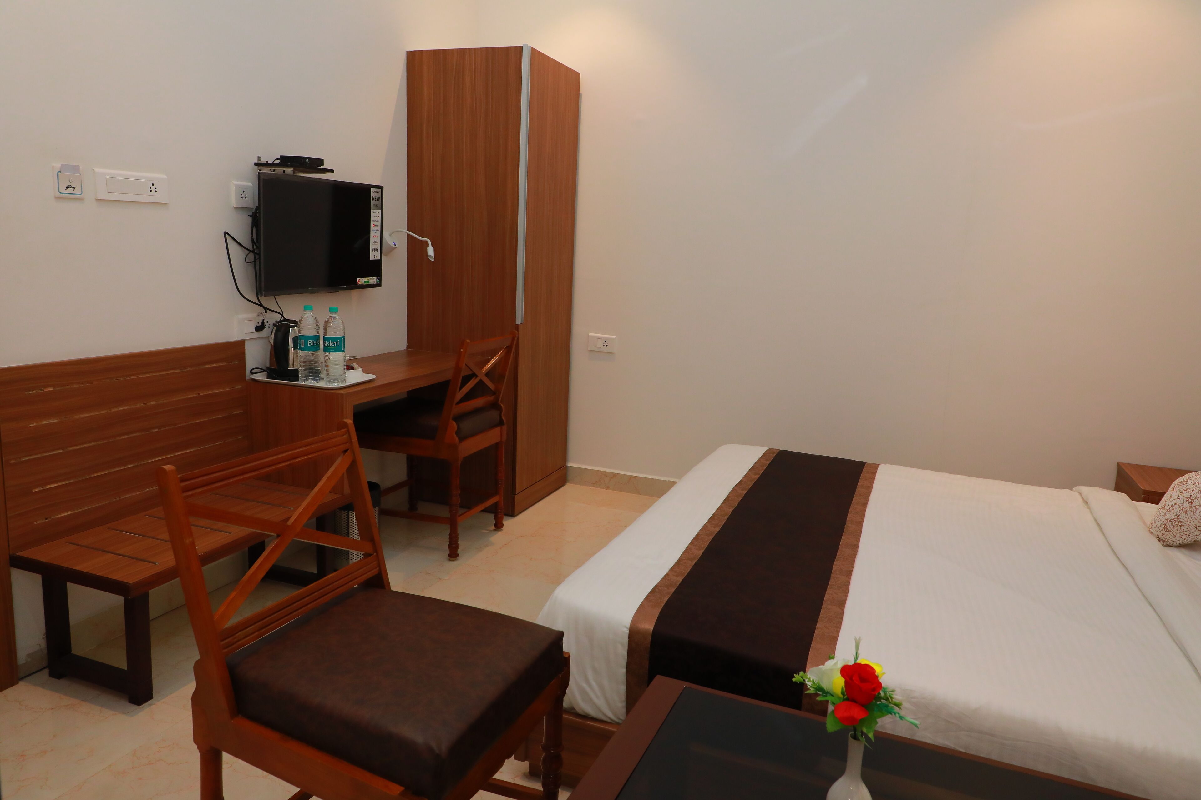 A hotel room with a bed, a desk with a chair, a television, and a small table with a vase of flowers.