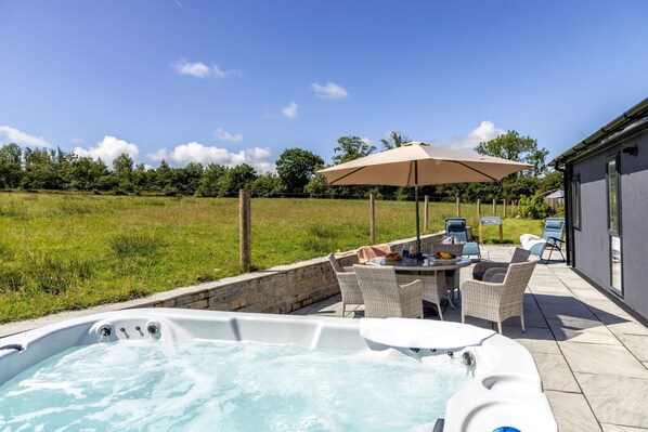 Un bain à remous avec une table et des chaises, un parasol et une vue sur un champ verdoyant.