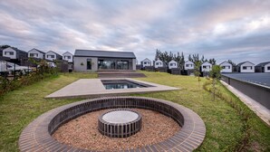 A modern residential area with houses, a central courtyard with a circular water feature, and a well-maintained lawn. - The Woods Luxury Homes - Elaleni Estate (Ballito)