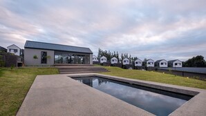 A modern residential area with a central building featuring large windows and a reflective pool. - The Woods Luxury Homes - Elaleni Estate (Ballito)