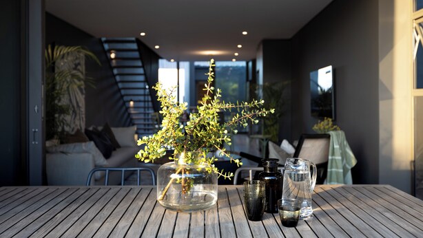 A modern dining area with a wooden table, a clear glass vase with a plant, and a pitcher. - The Woods Luxury Homes - Elaleni Estate (Ballito)