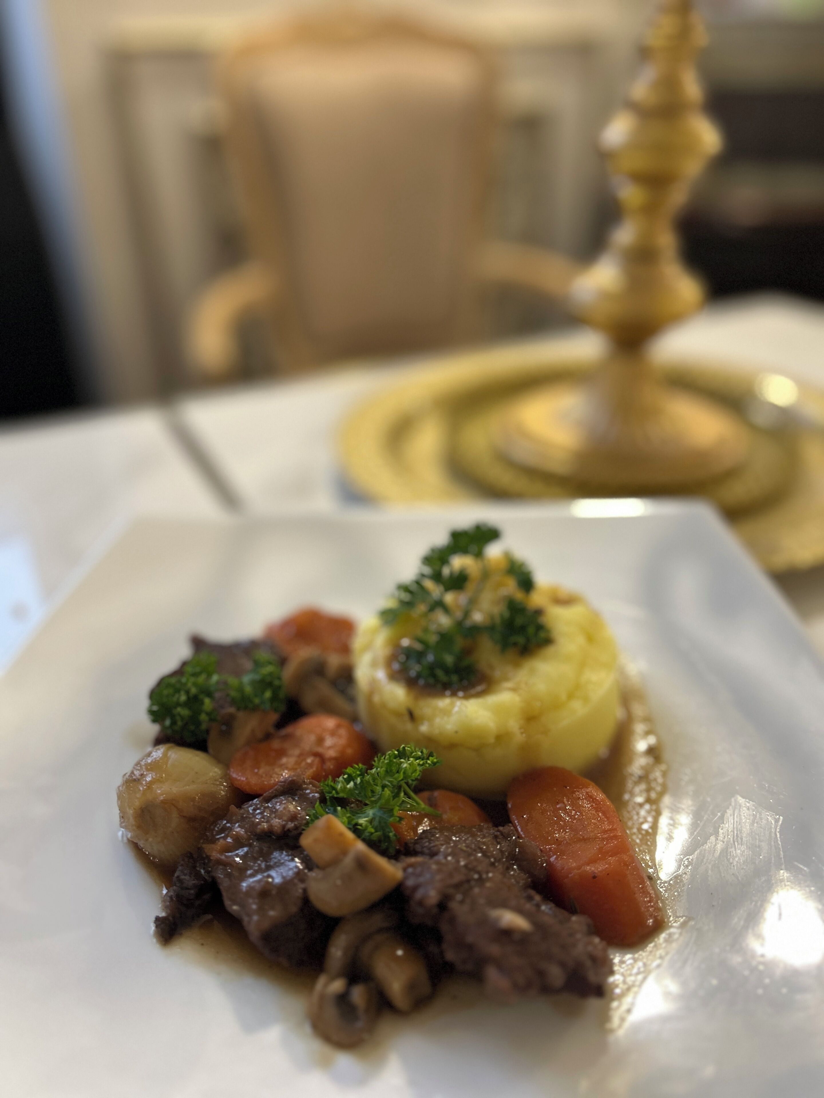 Un plato de comida con ternera, champiñones y zanahorias, decorado con perejil, sobre un plato blanco.
