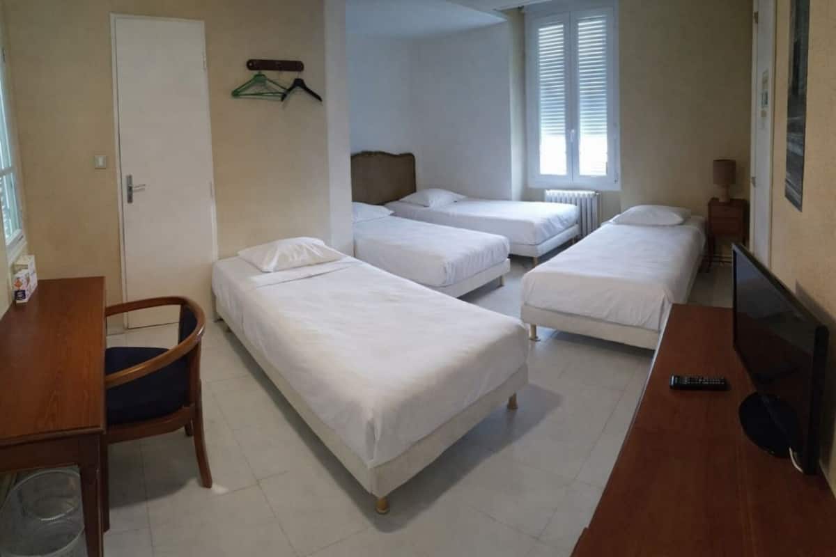 A hotel room with three single beds, a wooden desk, a chair, a television, and a radiator.