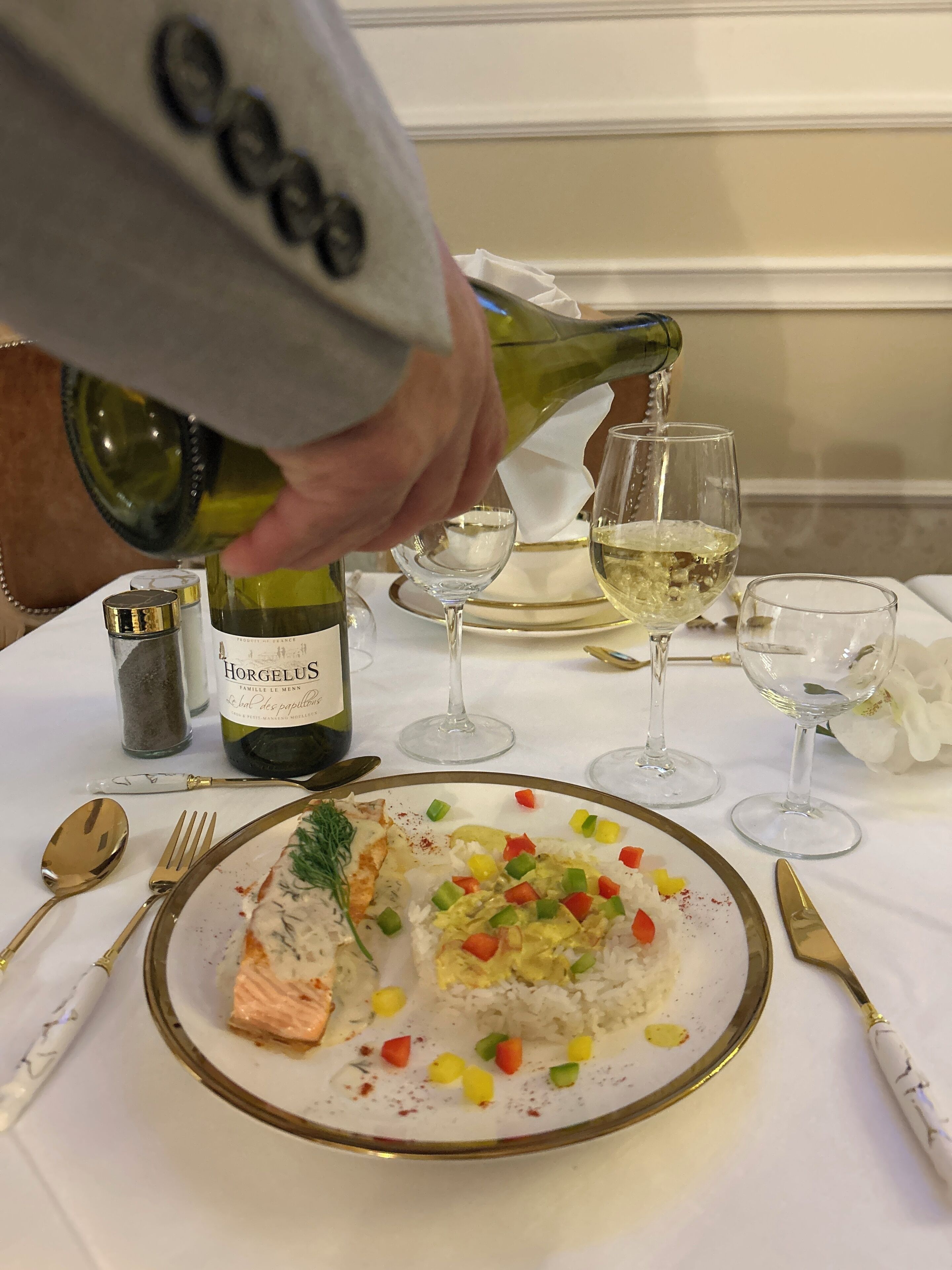 A dining table with a plate of food, a bottle of wine, and a wine glass.
