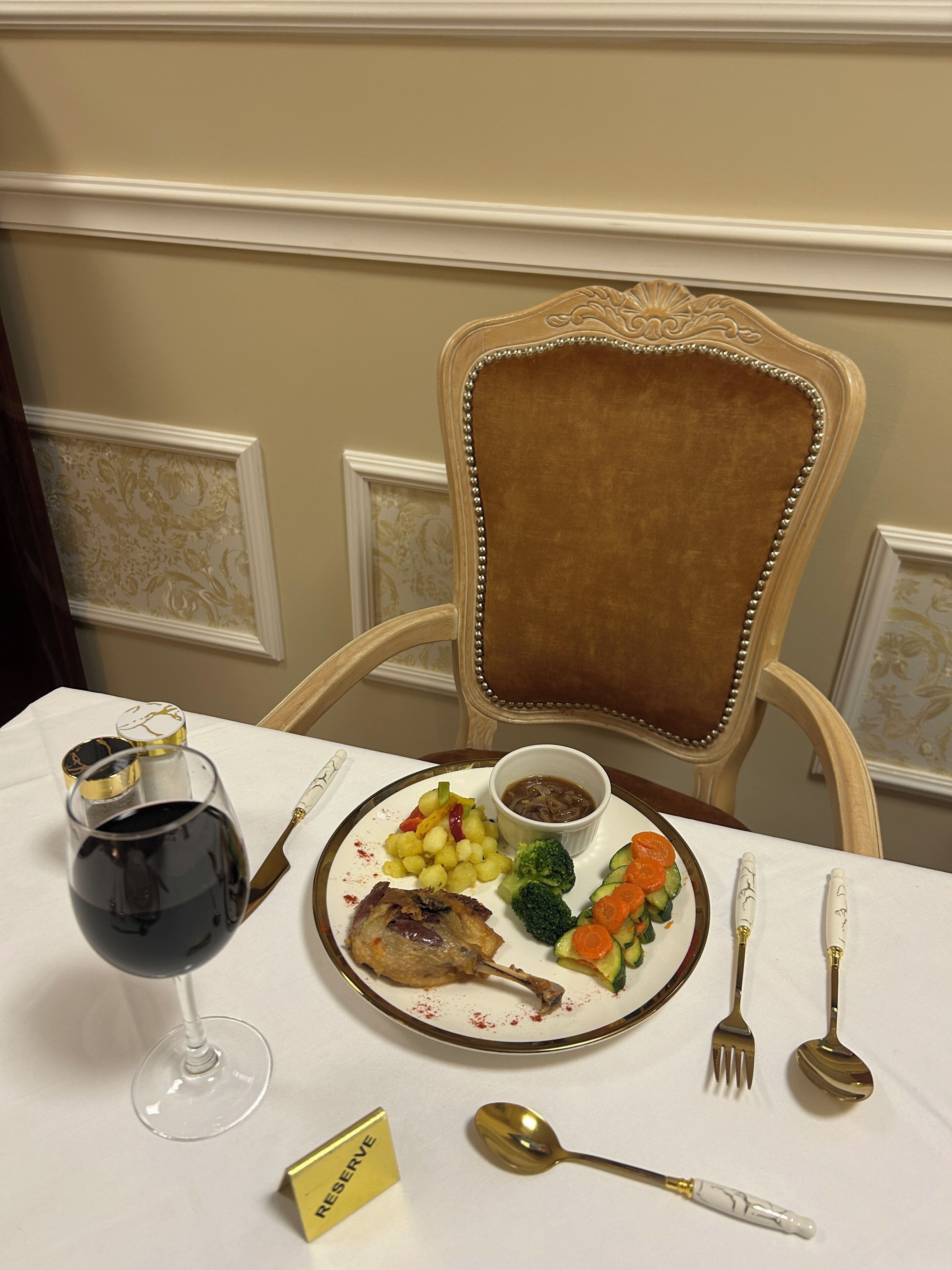 A dining table with a plate of food, a glass of red wine, and cutlery.