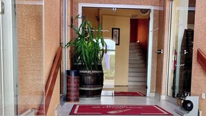 Entrada de hotel con alfombra roja, plantas en macetas y una escalera que da al interior.
