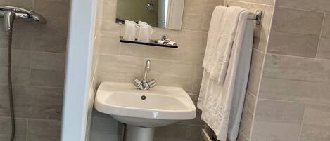 A bathroom with a pedestal sink, a mirror, a towel rack, and a shower.