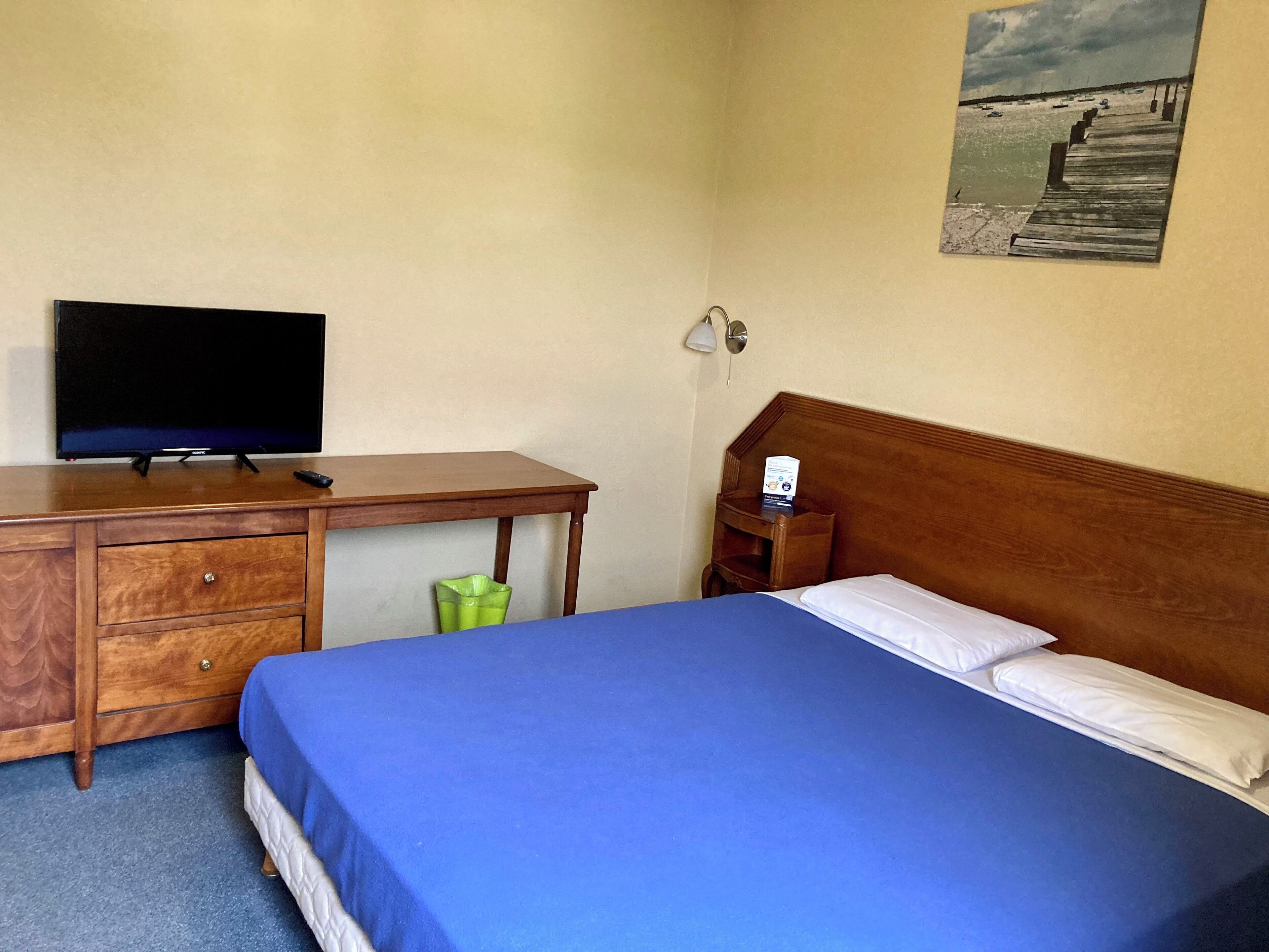 Una habitación de hotel con una cama, un escritorio con televisor, una mesita de noche y una lámpara de pared.