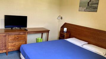 Una habitación de hotel con una cama, un escritorio con televisor, una mesita de noche y una lámpara de pared.