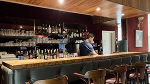 Un área de bar con mostrador, taburetes y estantes llenos de botellas y vasos.
