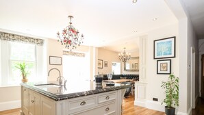 A spacious kitchen with a large island, wooden flooring, and a chandelier. - The Farmhouse (North Walsham)