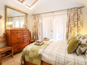 A bedroom with a bed, a wooden dresser, a chair, a mirror, and a window with curtains. - The Farmhouse (North Walsham)