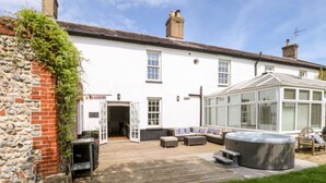 A white house with a wooden deck, a hot tub, and a conservatory. - The Farmhouse (North Walsham)