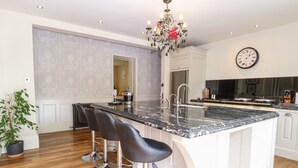 A modern kitchen with a marble countertop, stainless steel appliances, and a chandelier. - The Farmhouse (North Walsham)