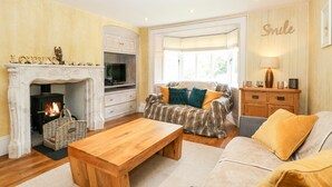 A cozy living room with a fireplace, a sofa, a coffee table, and a television. - The Farmhouse (North Walsham)