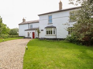 A white two-story house with a red door, a gravel driveway, and a well-maintained lawn. - The Farmhouse (North Walsham)