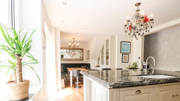 A modern kitchen with a large island, white cabinetry, and a chandelier. - The Farmhouse (North Walsham)