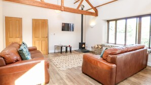 A cozy living room with leather sofas, a fireplace, wooden beams, and a large window. - The Barnhouse (North Walsham)