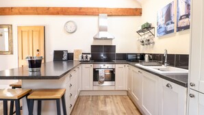 A modern kitchen with wooden beams, a black countertop, white cabinets, a built-in oven, and a sink. - The Barnhouse (North Walsham)