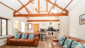 A spacious living area with a high ceiling and exposed wooden beams, furnished with leather sofas and a woven rug. - The Barnhouse (North Walsham)