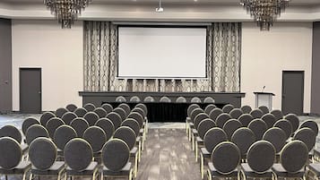 Ett konferensrum med rader av stolar, en stor skärm och två kristallkronor.
