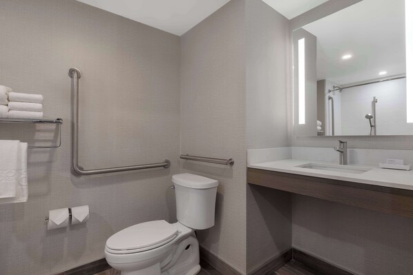 Un baño moderno con inodoro, barras de apoyo, lavabo y espejo.