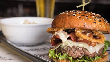 Un hamburger servi sur un plateau, avec un pain aux graines de sésame, du bacon, du fromage et de la laitue.