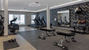 Een moderne sportschool met loopbanden, elliptische trainers, een bank, gewichten en een spiegel die de apparatuur weerspiegelt.