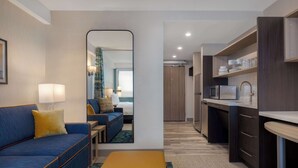 Een compacte hotelkamer met een bank, een klein tafeltje, een spiegel, een kitchenette en een badkamer die door een open deur zichtbaar is.