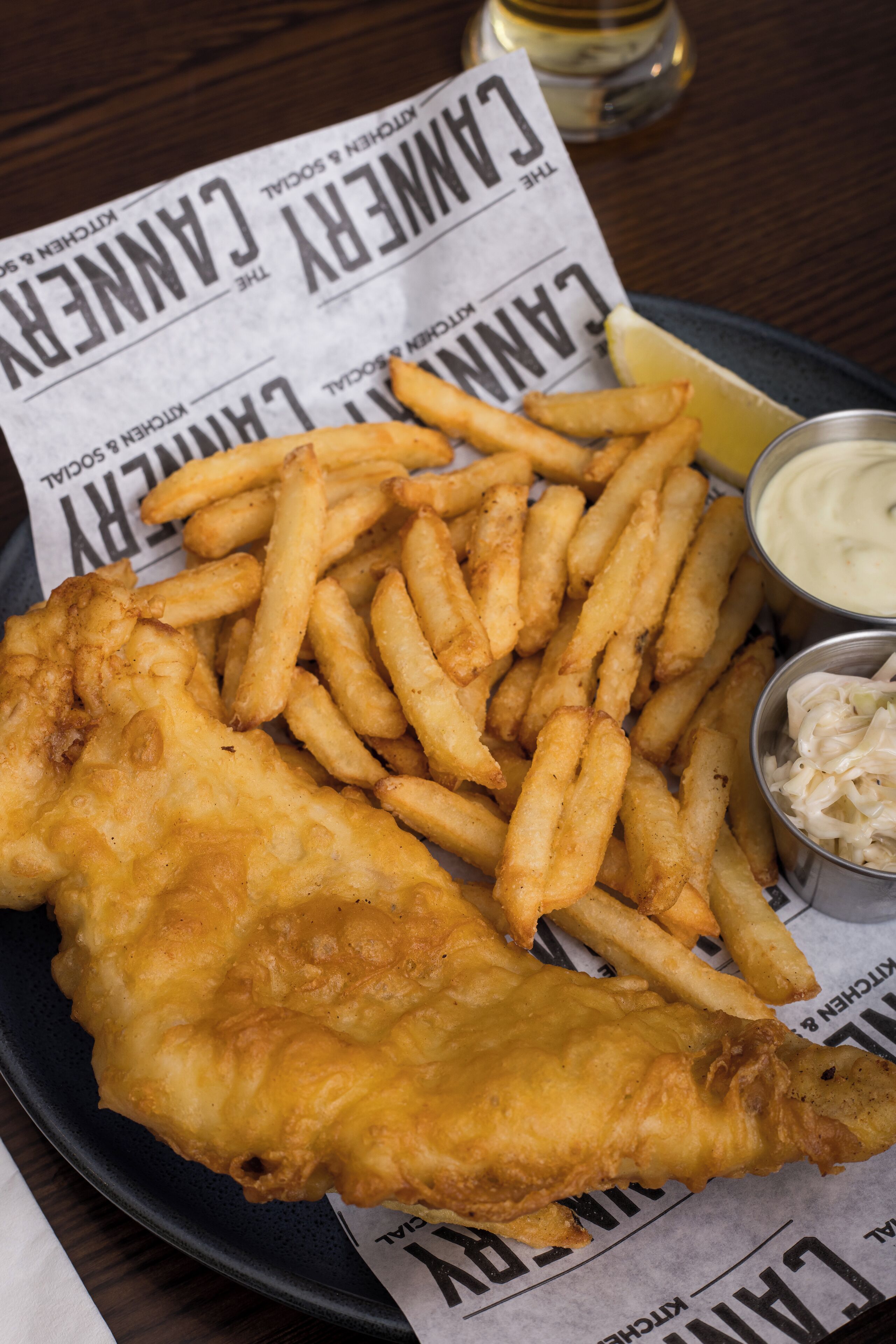 A plate of fish and chips with a lemon wedge and two dipping sauces.